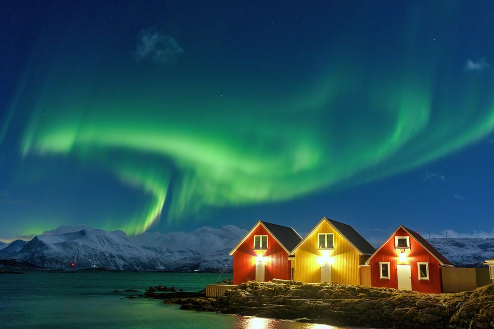 aurora borealis over snowcapped mountains and fishermen cabins by the sea, sommaroy, troms og finnmark, norway