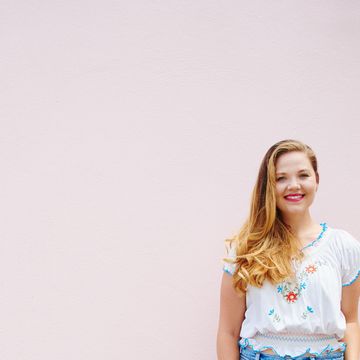 shot of a beautiful young woman posing against a pink wall outside