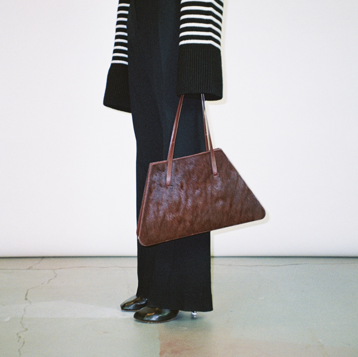 a person wearing a black and white sweater and holding a burgundy purse to illustrate a guide to the best designer tote bags of 2024
