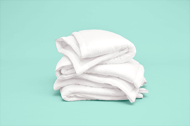 folded stack of good housekeeping best comforters on a blue background