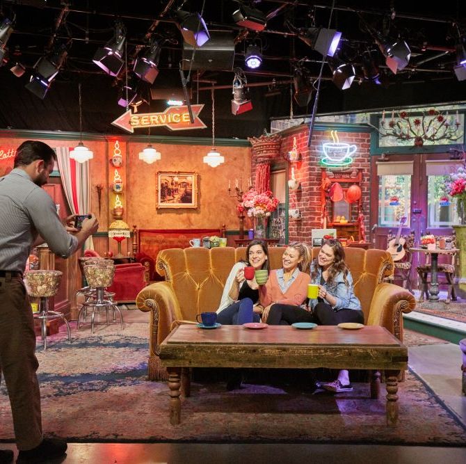 three visitors posing on the central perk couch as part of the warner bros studio tour, a good housekeeping pick for best factory tours