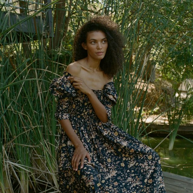a model wears a doen floral dress in front of greenery to illustrate a guide to the best fall dresses for 2023