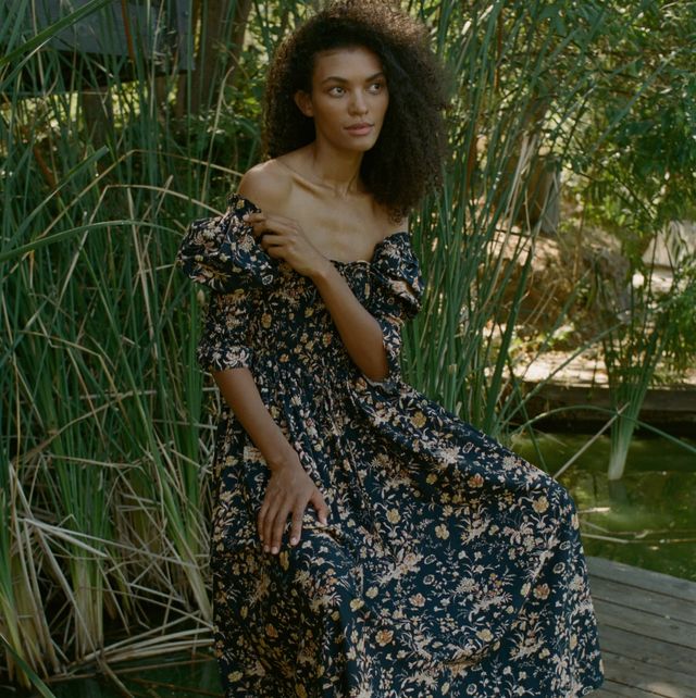 a model wears a doen floral dress in front of greenery to illustrate a guide to the best fall dresses for 2023