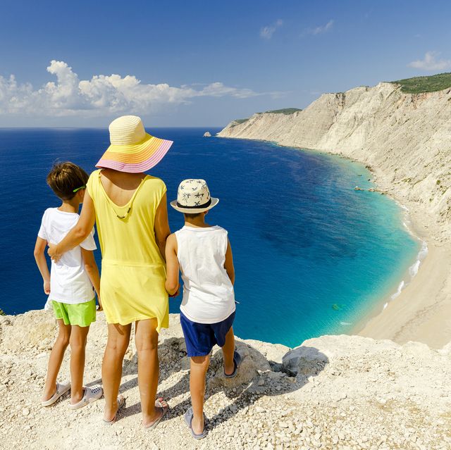 mother and sons embracing admiring the idyllic ammos beach standing on top of cliffs, kefalonia, ionian islands, greece