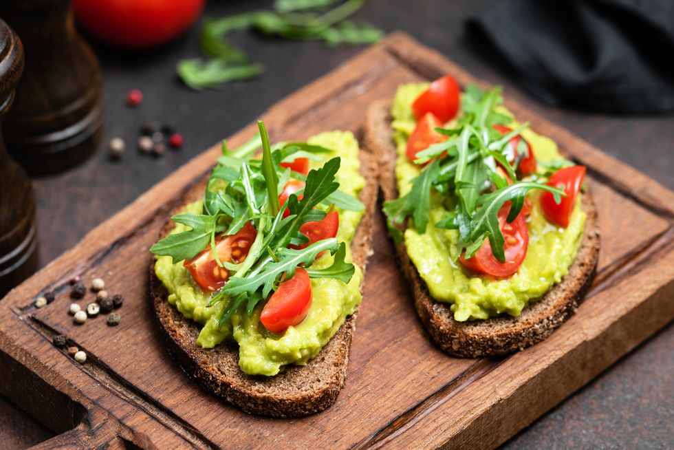 toast with mashed avocado, arugula served on wooden board