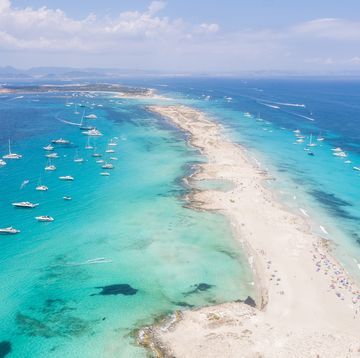 aerial overhead view of large amount of yachts anchored off the coast of formentera ibiza, with turquoise mediterranean sea and ocean blue water