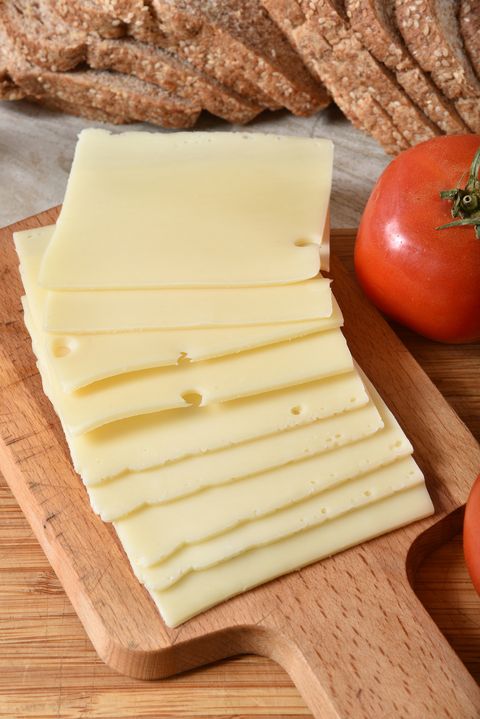 slices of swiss cheese on a cutting board with a tomato and whole wheat bread