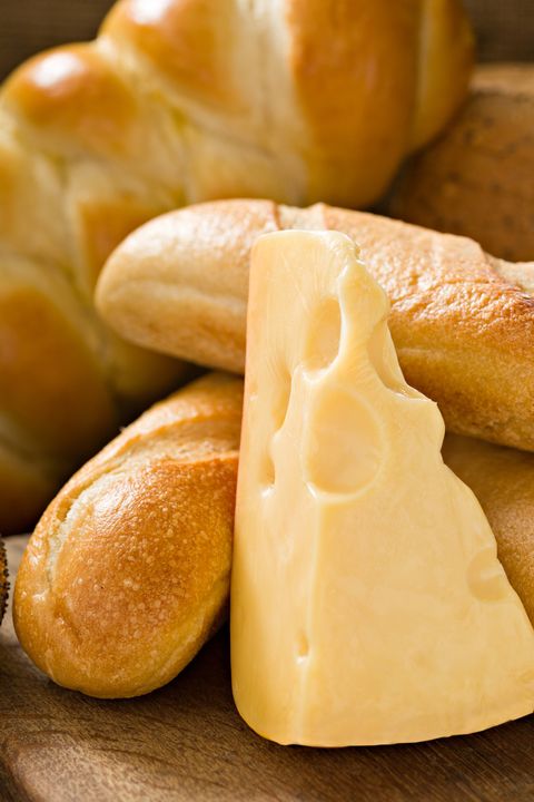 a close up shot of several loaves of bread and a chunk of jarlsberg cheese on an old wooden cutting board