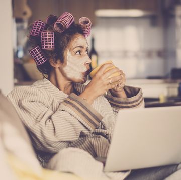 woman with hair rollers in drinking tea on sofa with laptop