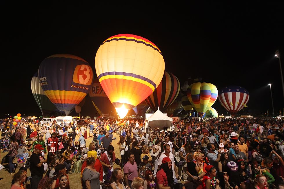 crowd, some in halloween costumes, gather around hot air balloons at spooktacular balloon festival in scottsdale at night