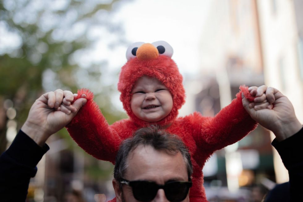 baby in furry red elmo costume rides on father’s shoulders at village halloween parade, new york city, a top halloween festival