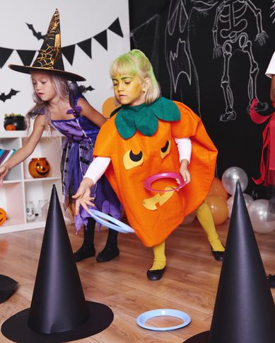 two girls dress as witch and pumpkin playing witch hat ring toss at a halloween party