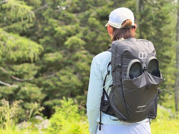 a woman looking out into a forest wearing a black backpack for hiking
