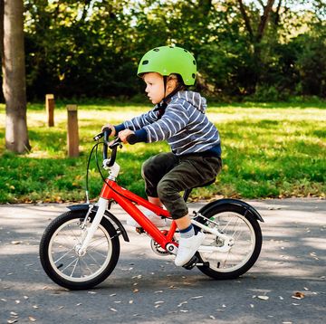 young child riding red bike with green helmet