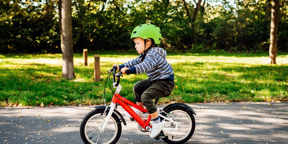 young child riding red bike with green helmet