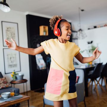 young happy african american girl dancing at home in her living room, wearing headphones, listening to music, having fun and learning the moves