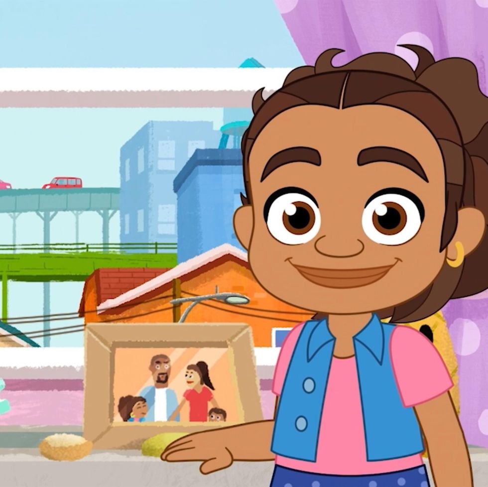 the 6 year old alma stands in front of a family photo in a scene from alma's way the show is a good housekeeping pick for best kids tv shows
