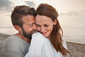 a man and woman standing on a beach at dusk snuggling and smiling