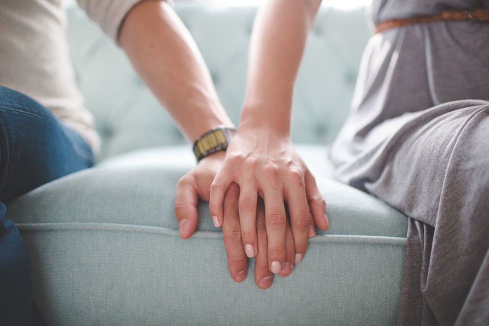 waist photo of man and woman holding hands while sitting on a couch her hand is on top of his hand