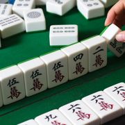 hand choosing a large mahjong tile on green felt board
