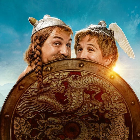 Astérix & Obélix smirk behind a shield in a promotional image for Astérix & Obélix: The Middle Kingdom, a Good Housekeeping pick for best kids' movies 2023 astérix obélix smirk behind a shield in a promotional image for astérix obélix the middle kingdom, a good housekeeping pick for best kids' movies 2023