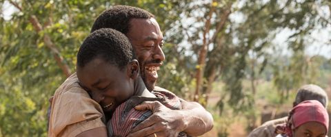 a father and son embrace happily in a scene from boy who harnessed the wind the movie is a good housekeeping pick for best kids movies on netflix