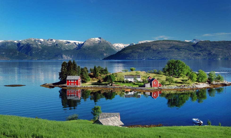 hardangerfjord in south western norway in the summer a red, norwegian house situated on a small island in the fjord in the distance the folgefonna glacier photo was taken near the village of omastranda