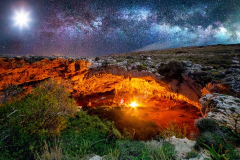 Klimmers in de Ghajn Tutagrot op Malta worden bijgelicht door het schijnsel van de maan en een oplaaiend kampvuur