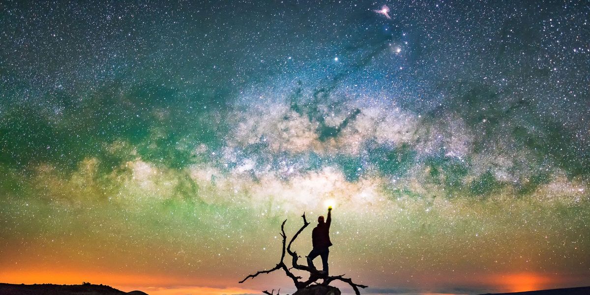 Onder de sterrenhemel boven de Mauna Kea op Hawa staat een man op een omgevallen boom