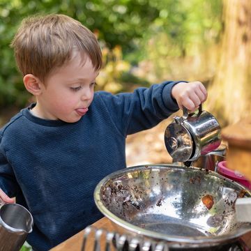 close up of a young boy playing outdoors with a mud kitchen