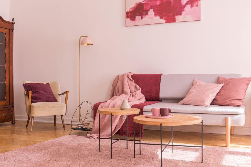 best paint colors, two coffee tables next to a grey sofa with pillows and blankets in a pastel pink living room interior