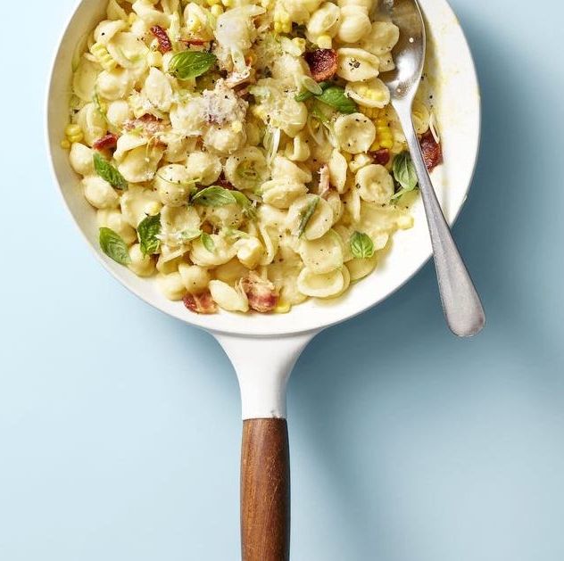 creamy corn pasta with bacon and scallions in a white skillet on a blue background