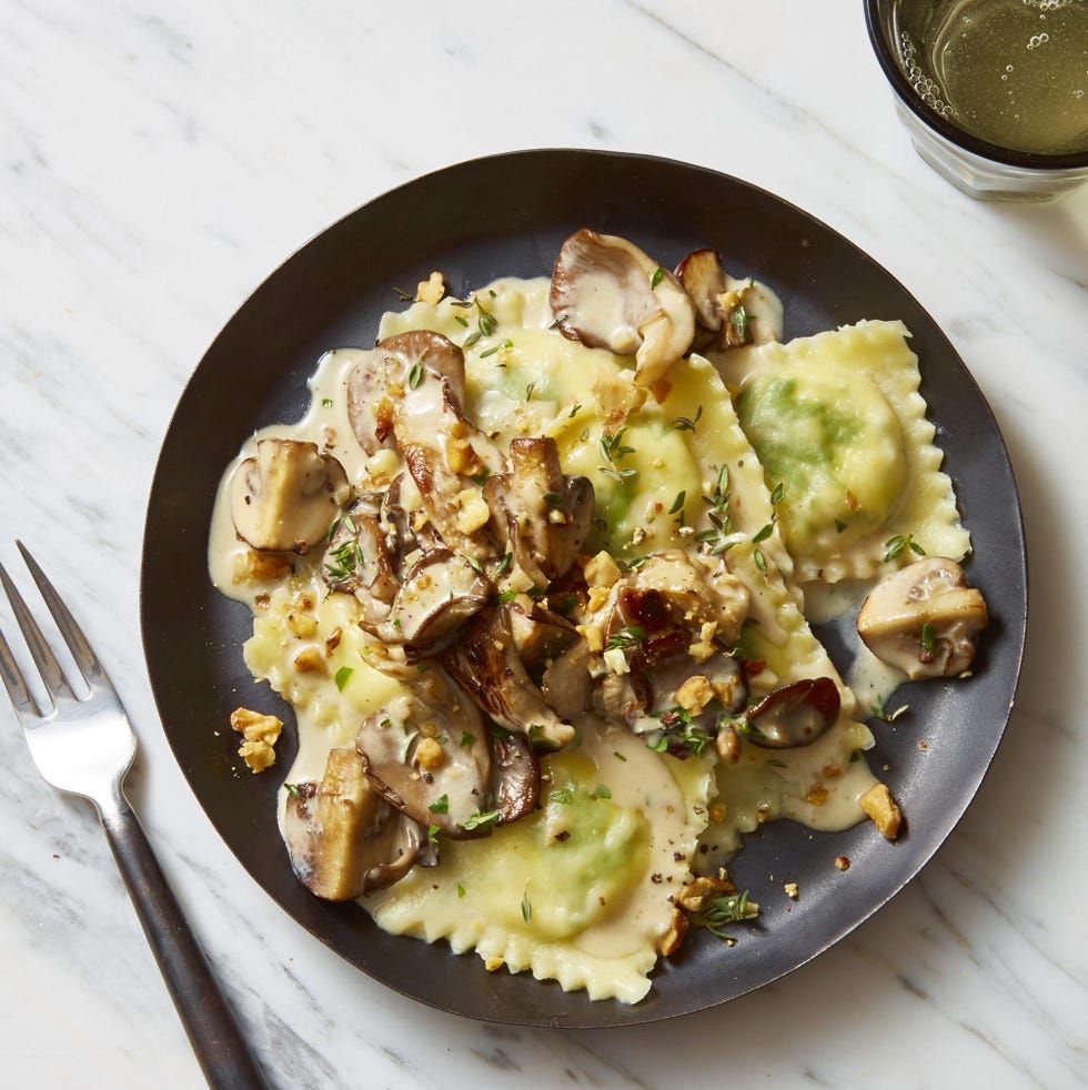 lemon ricotta ravioli with creamy herbed mushrooms on a black plate and marbled background
