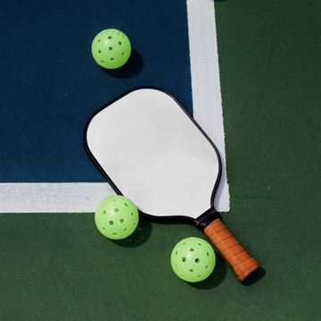 white pickleball paddle with lime green pickleballs laying on a court