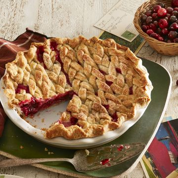 braided cranberry orange pie in a white pie dish with a pie server next to it and a green plate with a slice on it