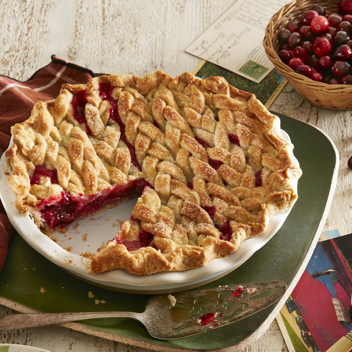 braided cranberry orange pie in a white pie dish with a pie server next to it and a green plate with a slice on it