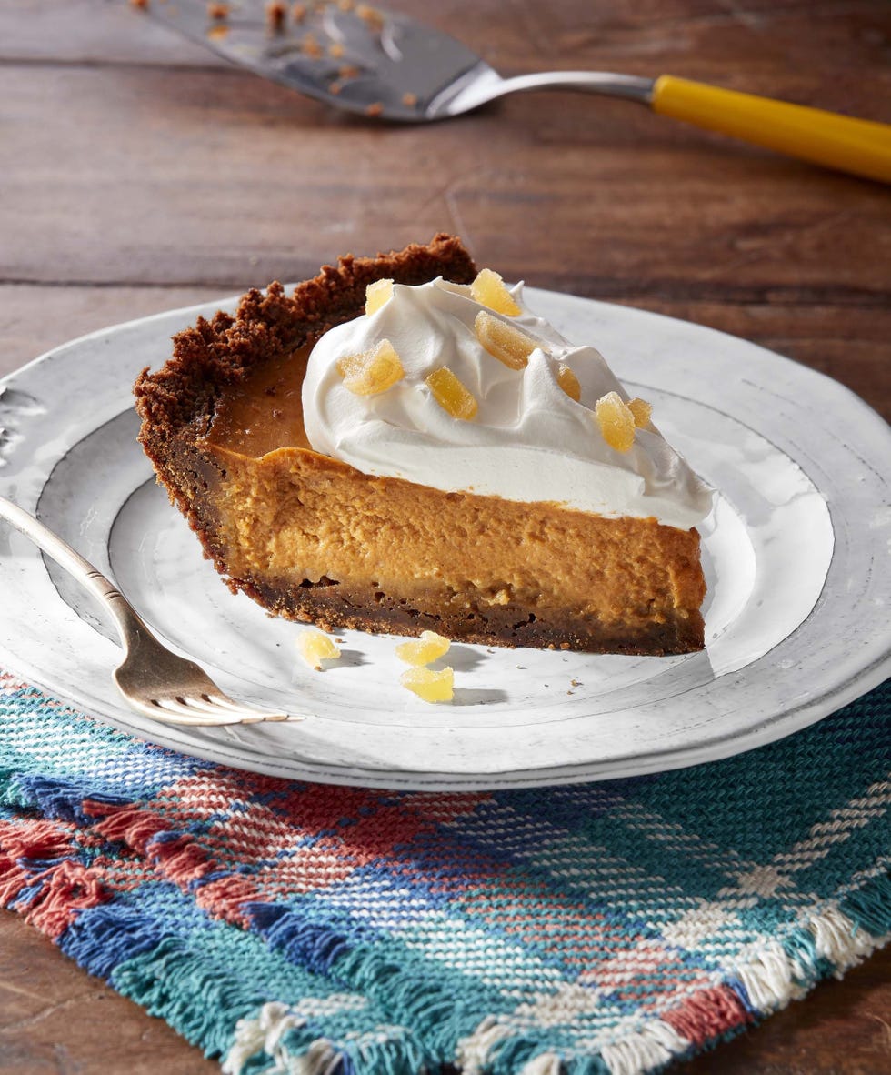 a slice of ginger pumpkin pie topped with whipped cream and candied ginger on a white plate with a fork