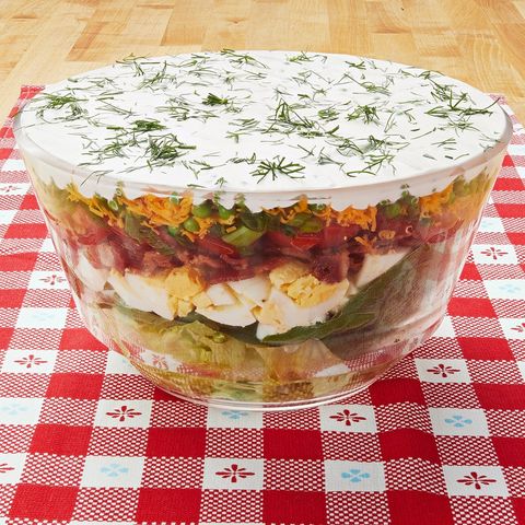 layered salad in big glass bowl with red and white tablecloth