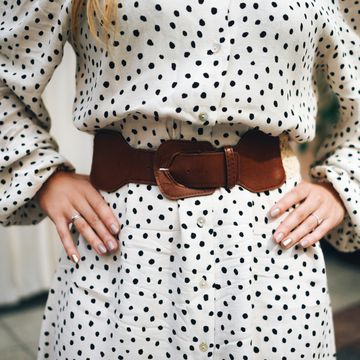 crop of woman in white and black polka dot dress with tan belt