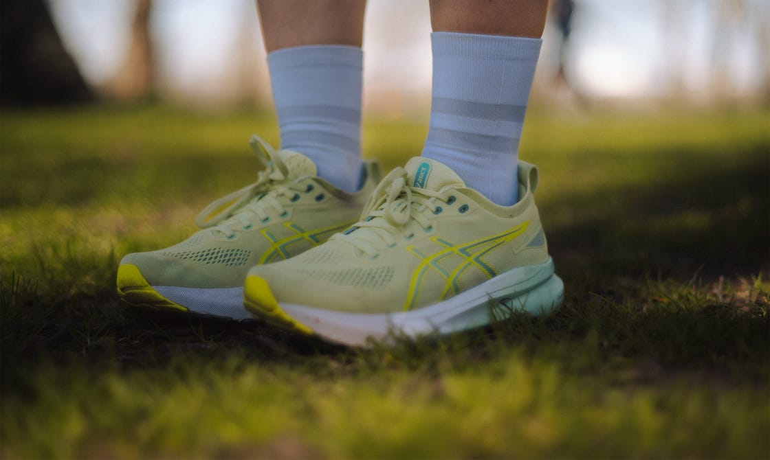a pair of legs wearing green asics running shoes and white quarter length socks, stood on grass
