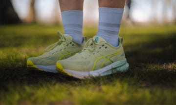 a pair of legs wearing green asics running shoes and white quarter length socks, stood on grass
