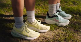 two pairs of legs stood on the grass showcasing their running shoes and quarter length running rocks
