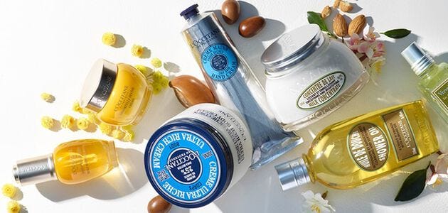 yellow, silver, blue and white l'occitane face and body skincare products on a white background with flowers and nuts