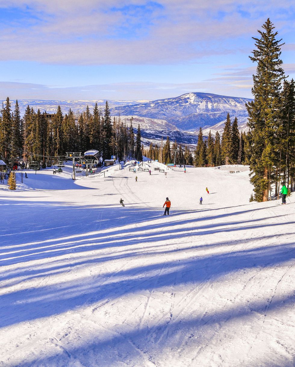 best ski resorts snowmass colorado, ski slope in late afternoon skiers and snowboarders skiing down