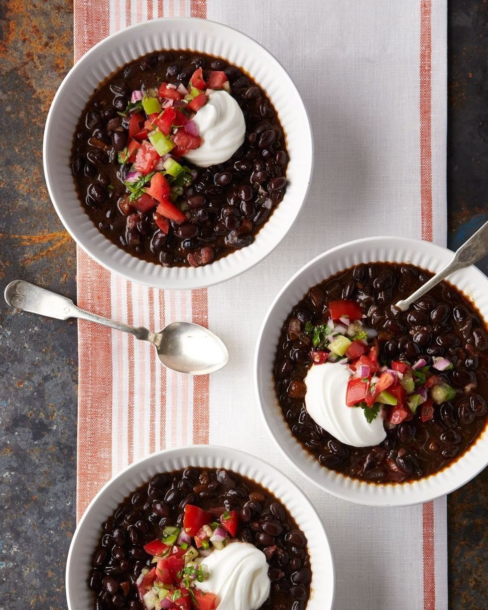 slow cooker black bean and chile soup pictured in three bowls and each topped with pico de gallo and a dollop of sour cream