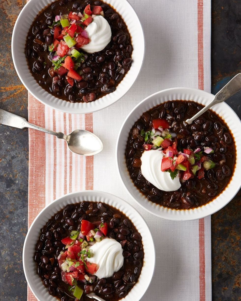 slow cooker black bean and chile soup pictured in three bowls and each topped with pico de gallo and a dollop of sour cream