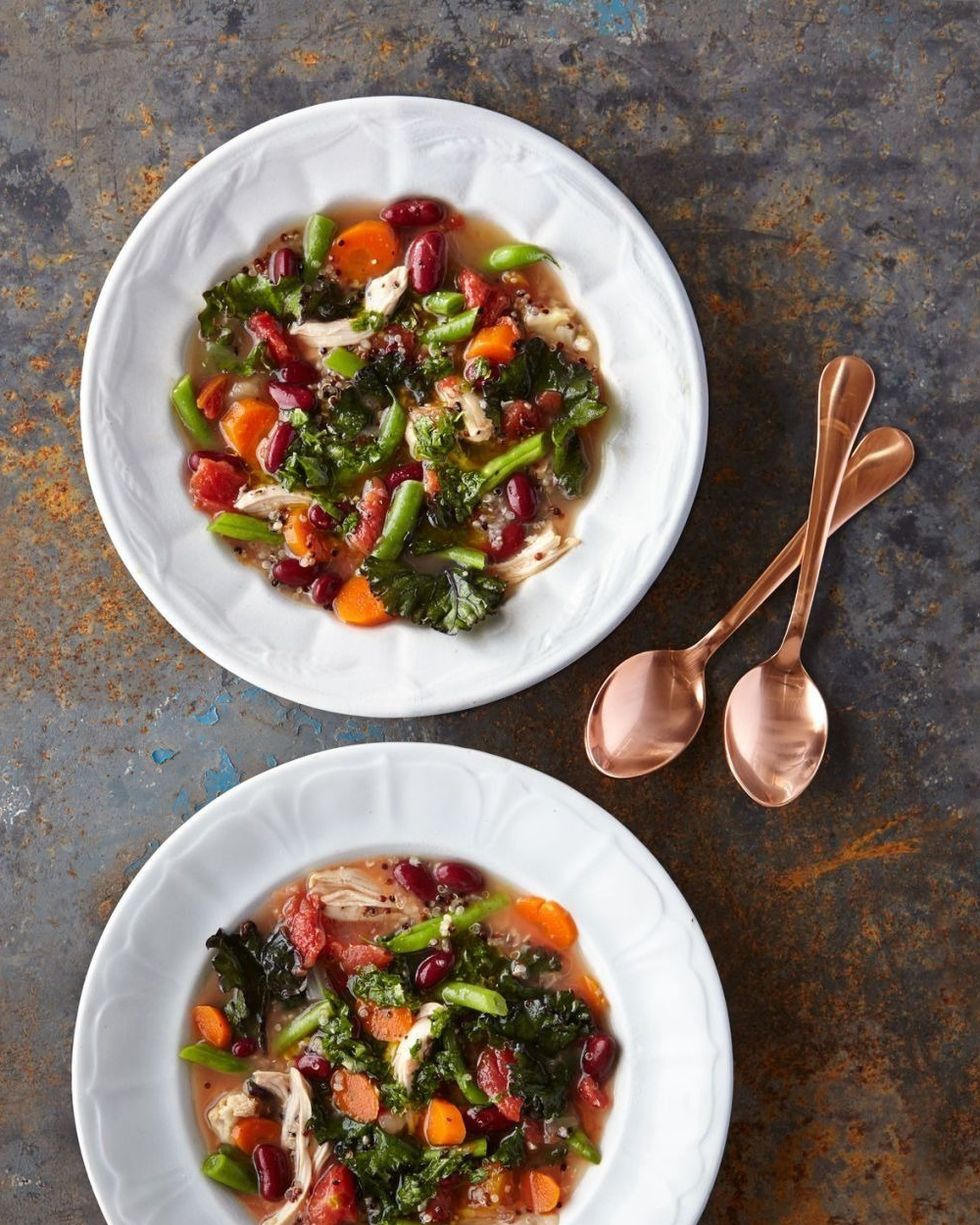 slow cooker chicken and quinoa minestrone in two white bowls with a copper spoon next to each
