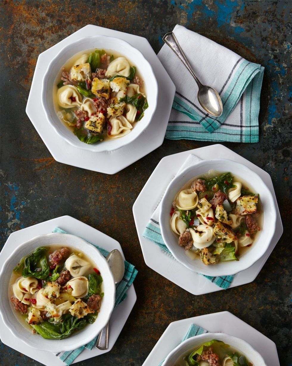 slow cooker sausage and tortellini soup in four white bowls with spoons