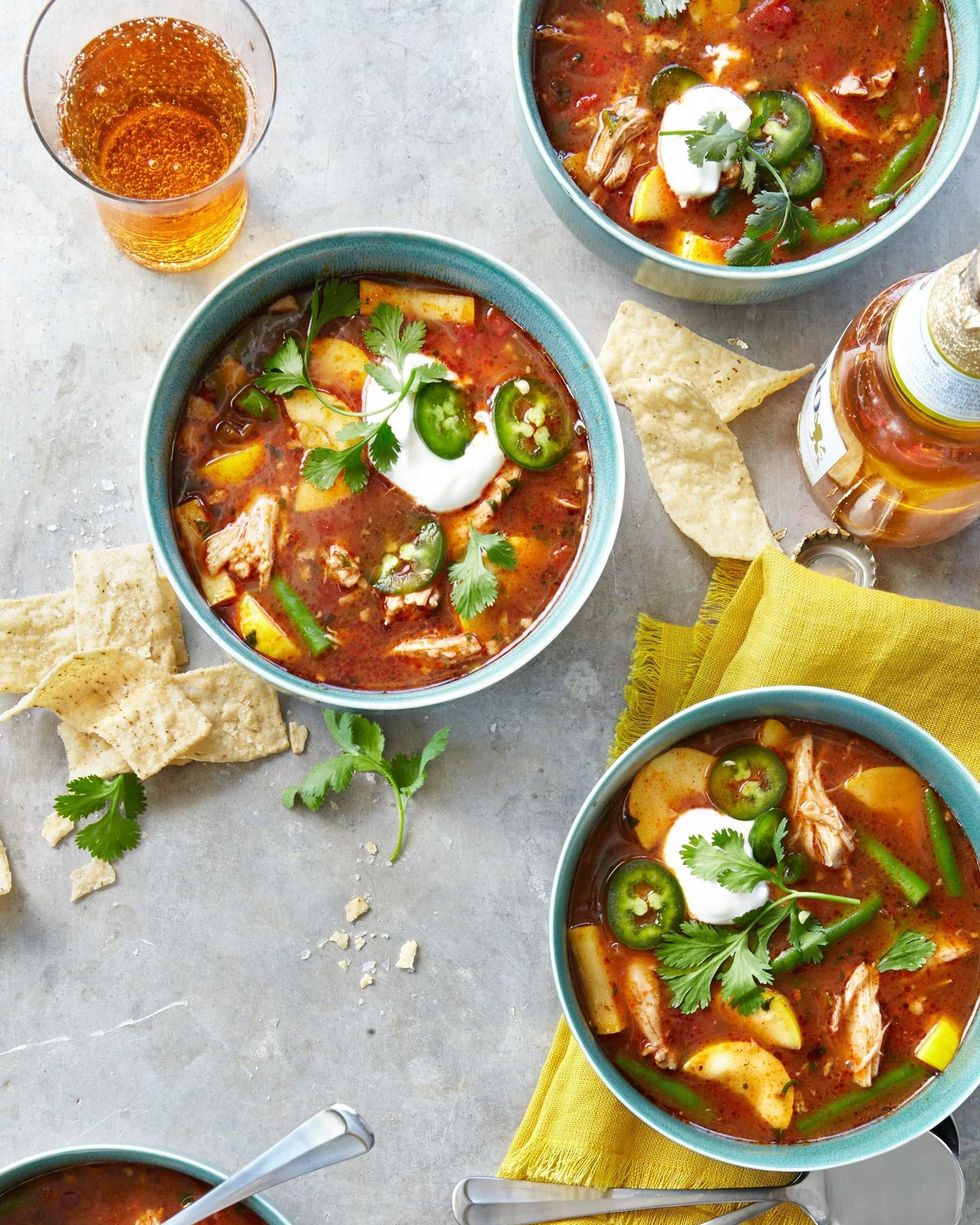 slow cooker chicken tortilla soup served in light teal bowls and topped with cilantro and sliced jalapenos and small dollops of sour cream