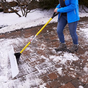 woman pushing snow shovel on brick patio